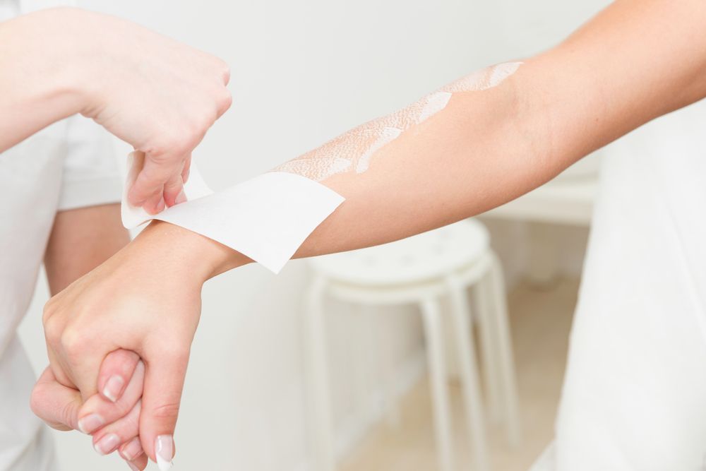 Person Waxing Arm With a White Strip in a Well-lit Room — Aspire Beauty & Nails in Wagga Wagga, NSW