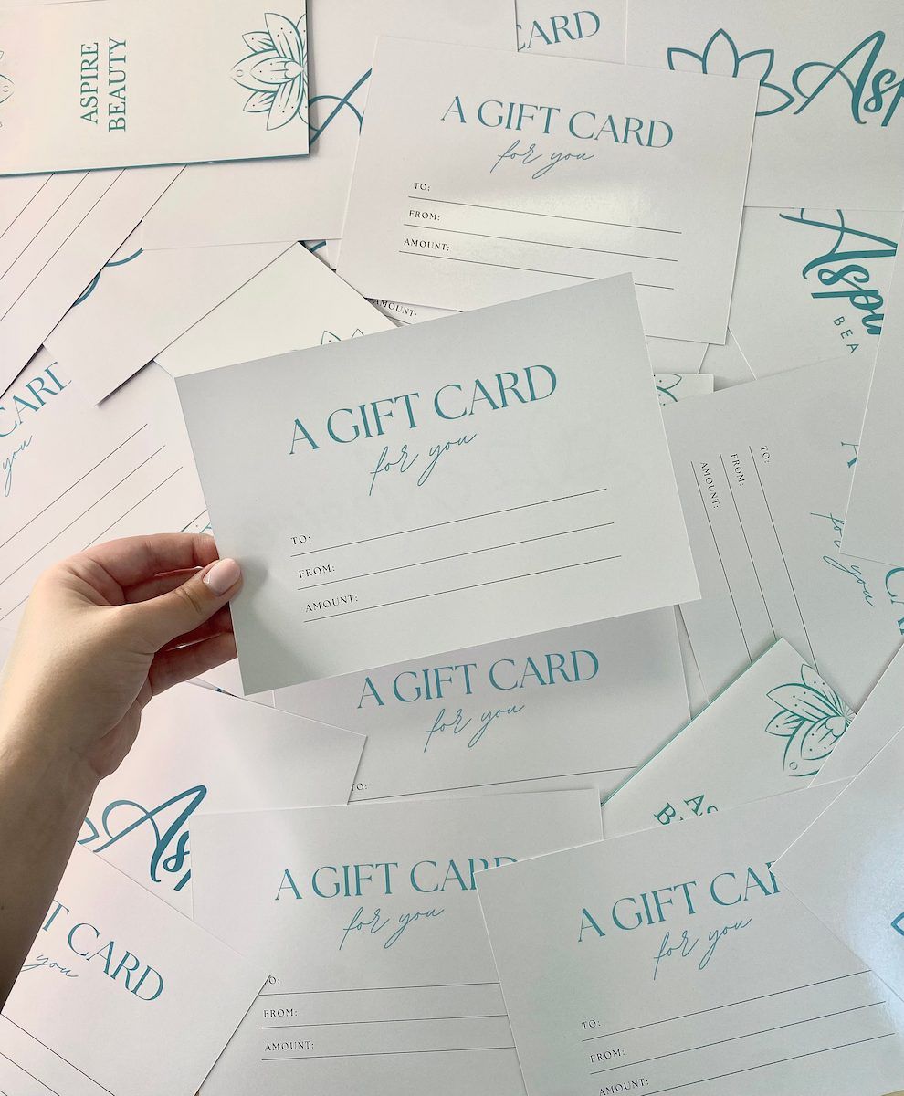 Hand Holding A White Gift Card Over A Pile Of Matching Teal — Aspire Beauty & Nails in Wagga Wagga, NSW