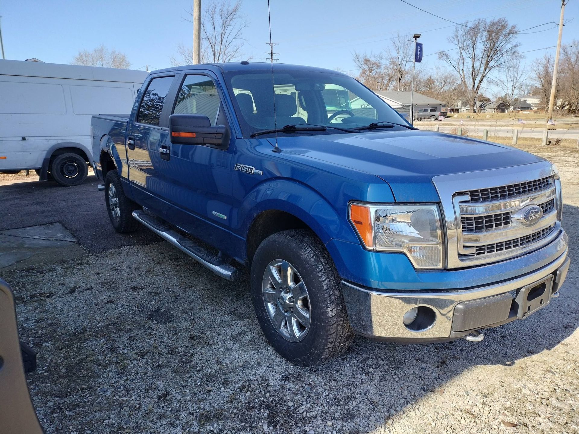 Blue Ford pickup truck parked on gravel lot in daylight
