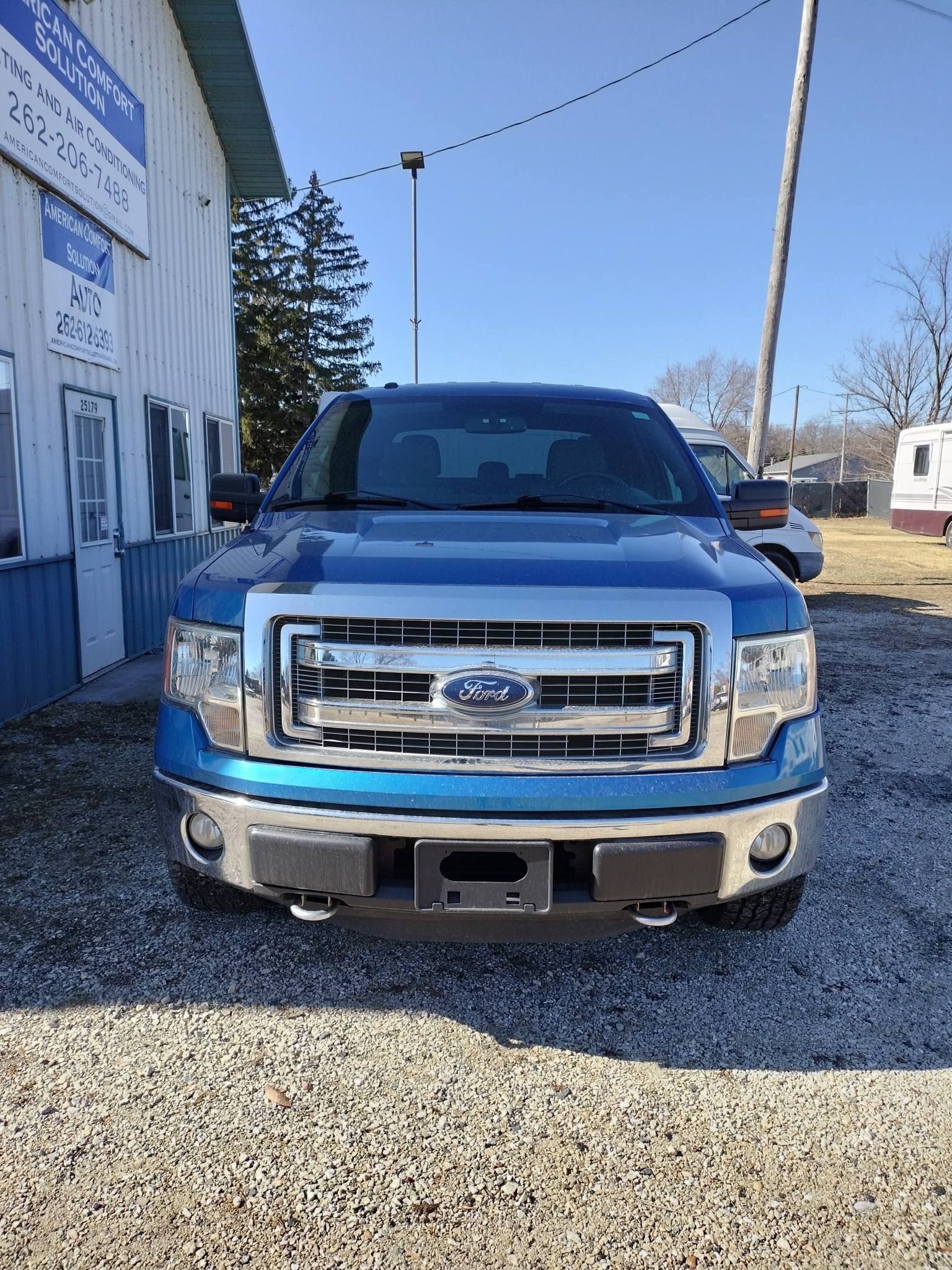Blue Ford pickup truck parked on gravel beside a building under a clear sky
