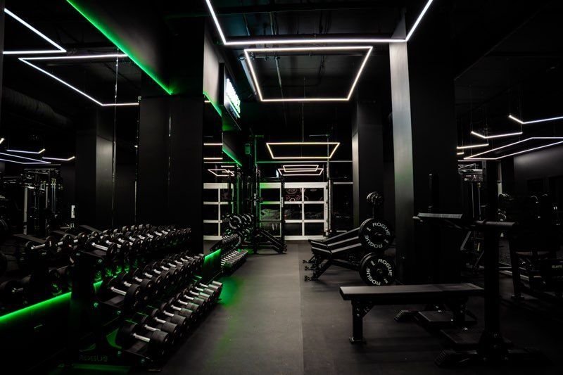 Une salle de sport avec beaucoup d'haltères et de lumières vertes.