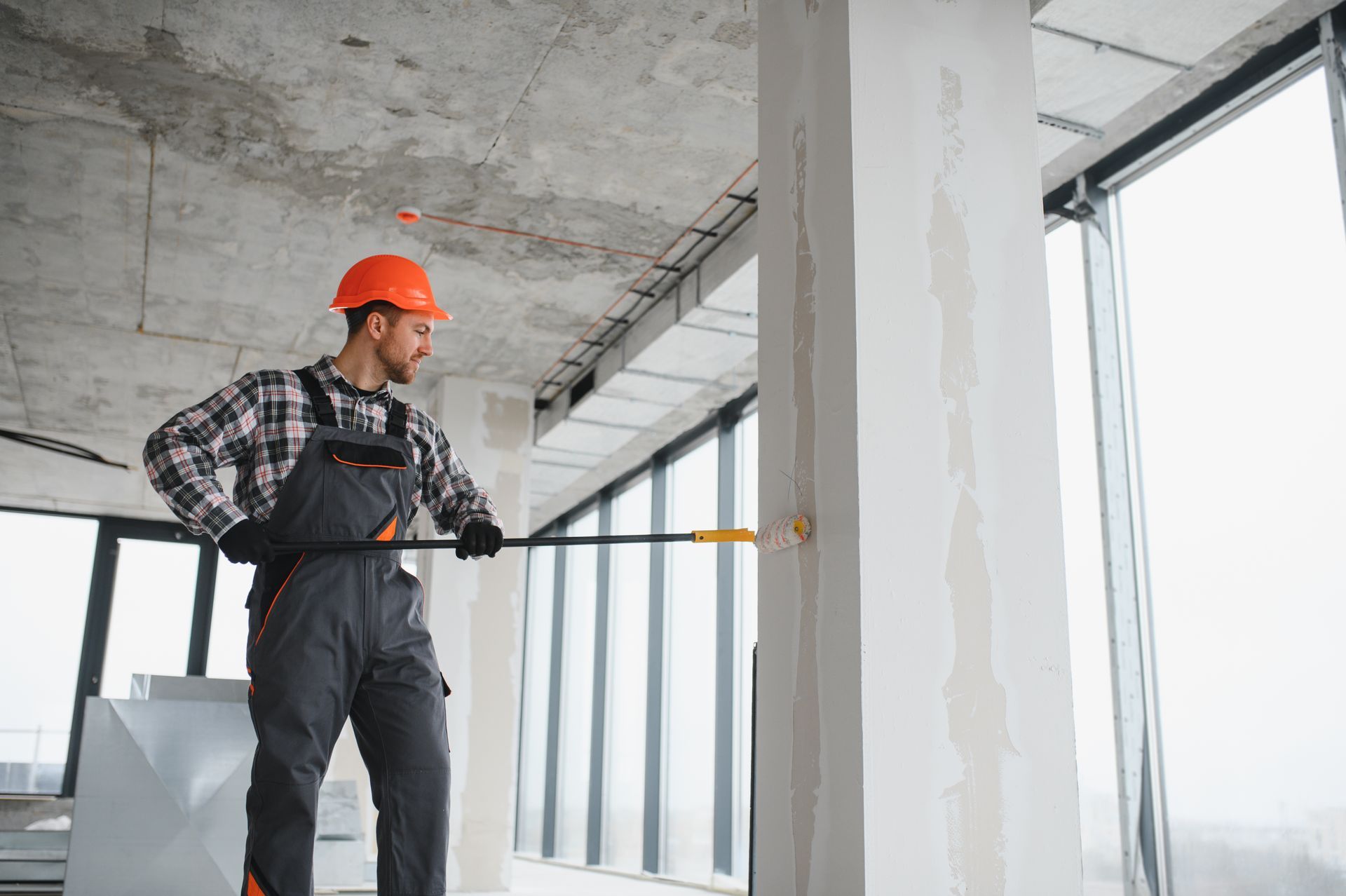 Construction worker in orange hard hat measuring a wall inside an unfinished building