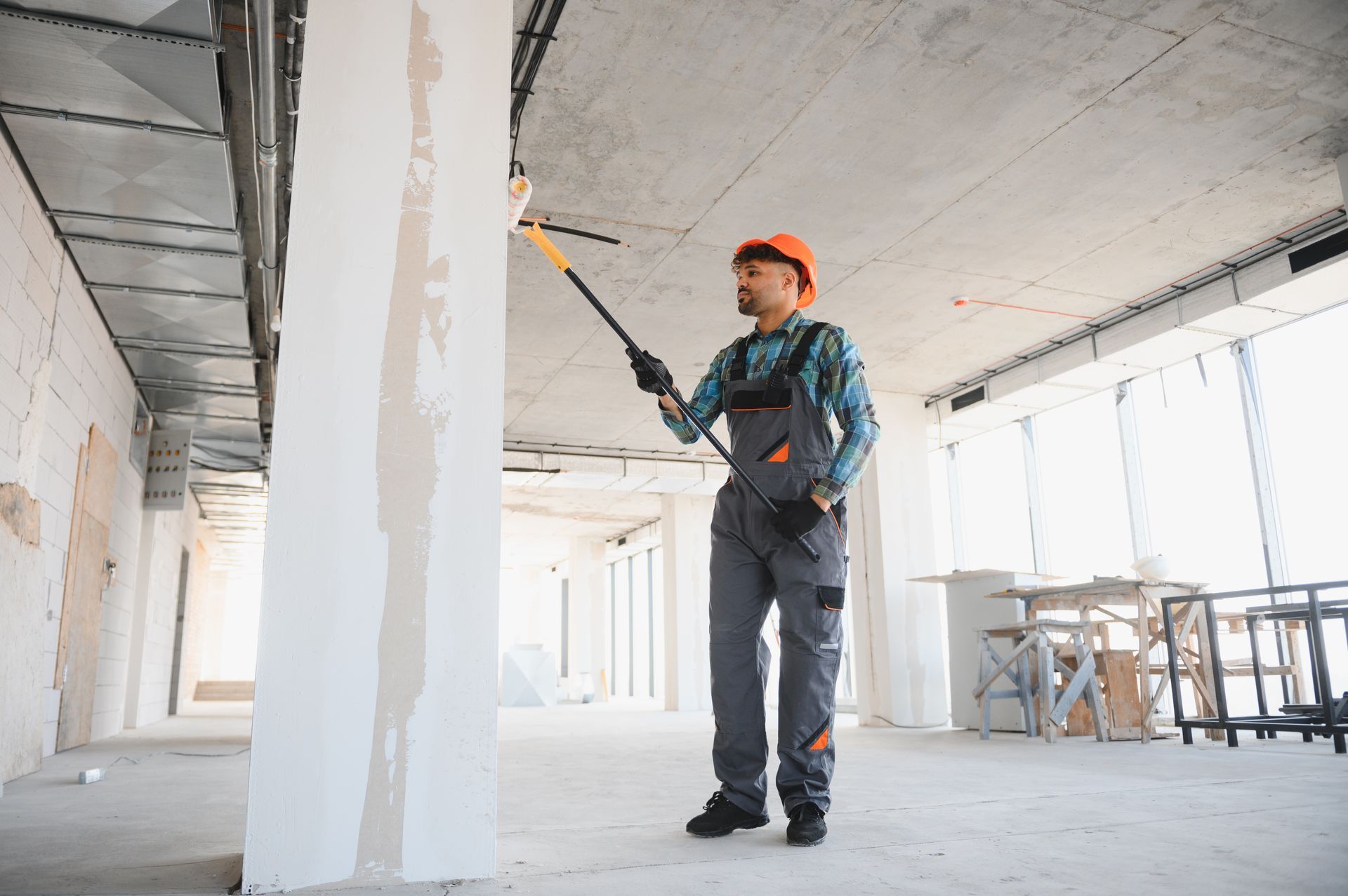 Worker painting a white column in an unfinished building interior.