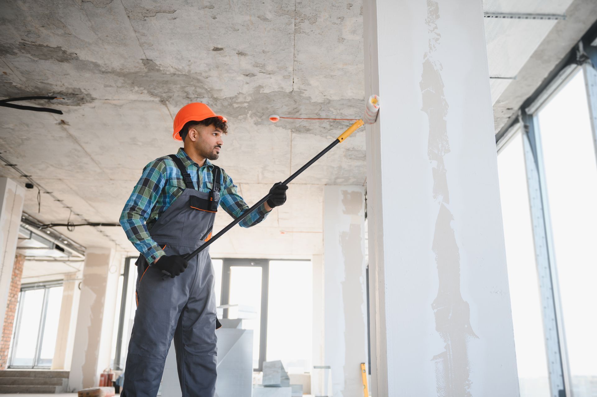 Worker in hard hat using a laser level inside an unfinished room under construction