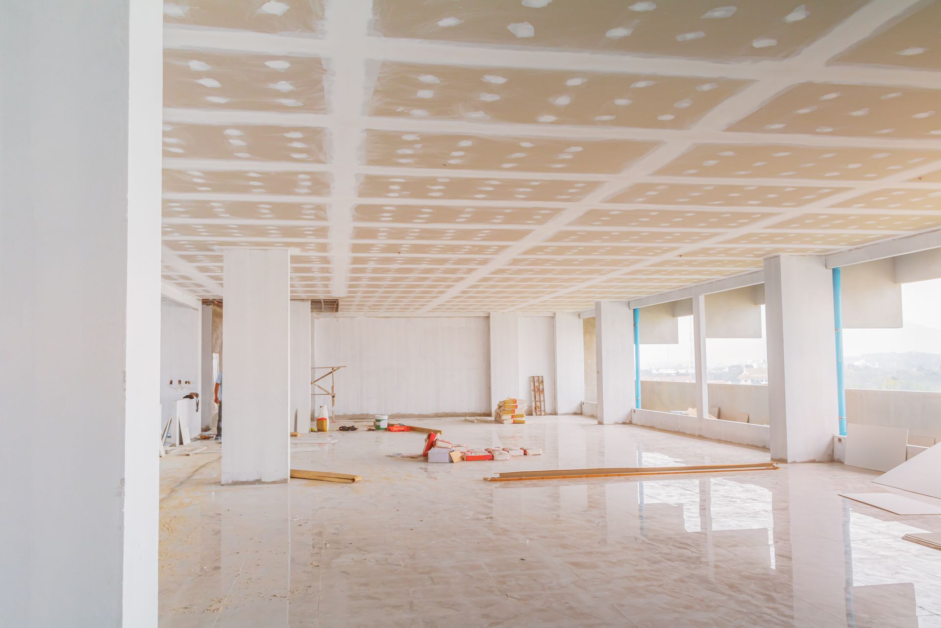 Empty unfinished room with white walls, columns, and tiled floor under renovation