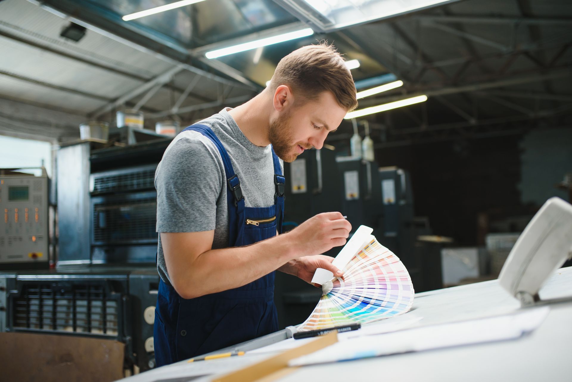 Technician in an apron examining a color swatch in a workshop beside a large white printer