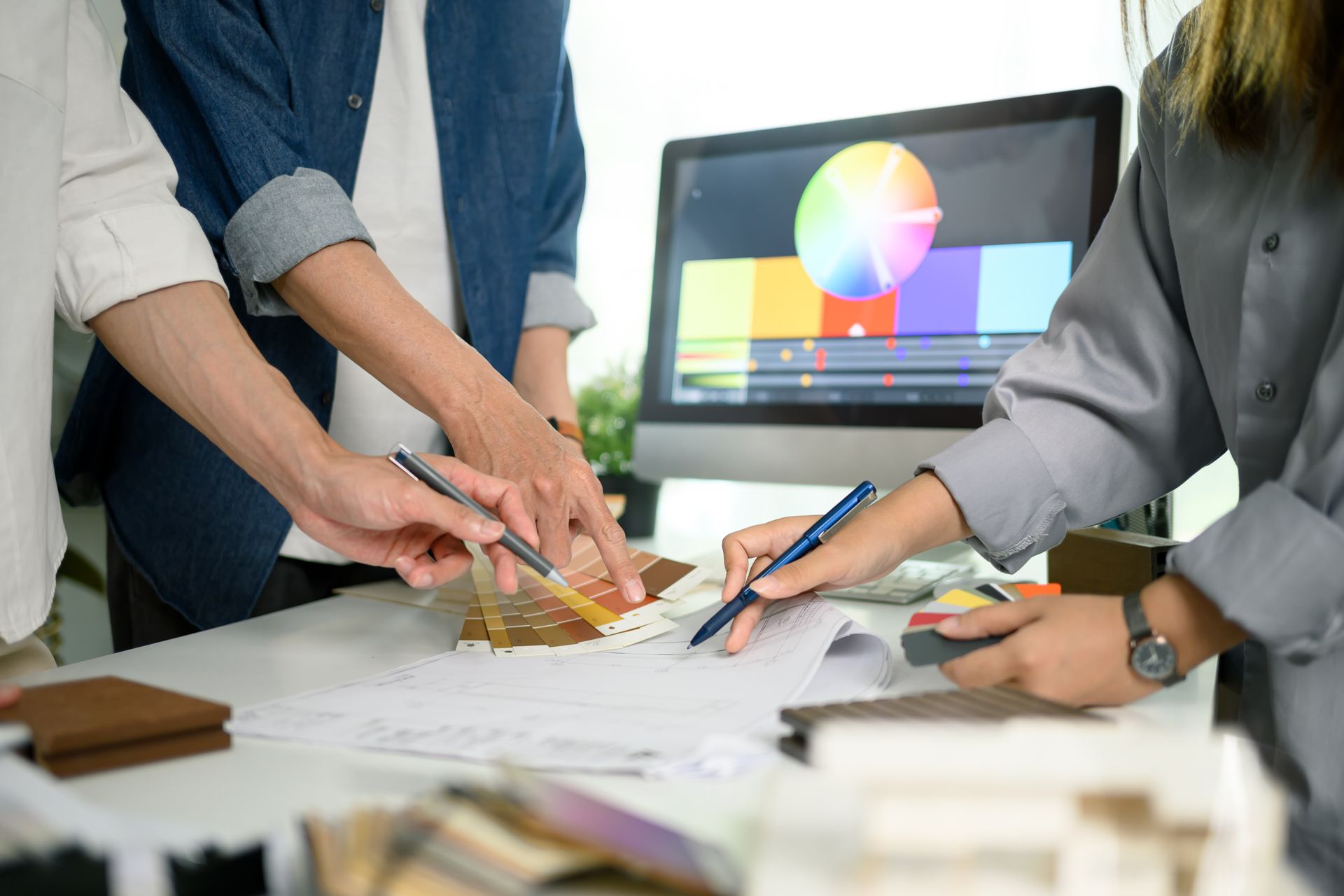 People collaborating around a desk, sketching designs beside a laptop displaying a color wheel.