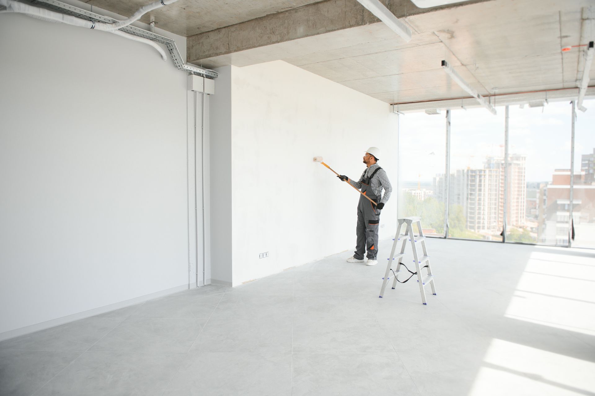 Worker inspecting a bright unfinished apartment interior with ladder and city view