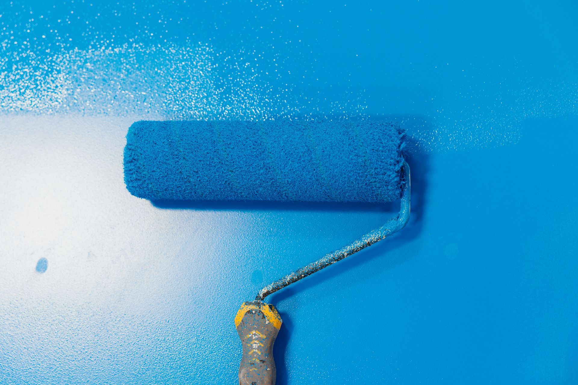 Blue paint roller painting a white wall blue