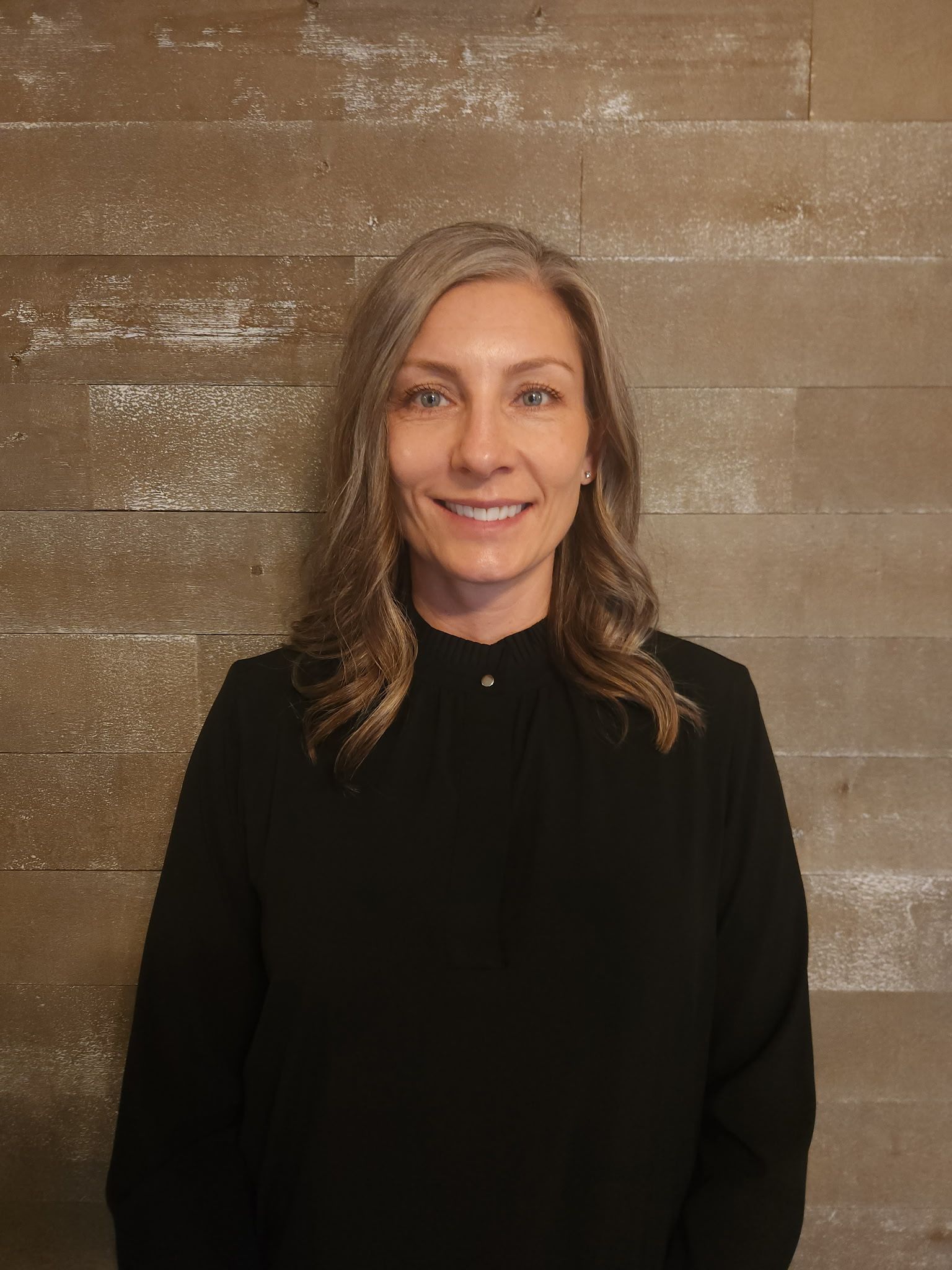 A woman in a sweater and vest is standing in front of a brick wall.