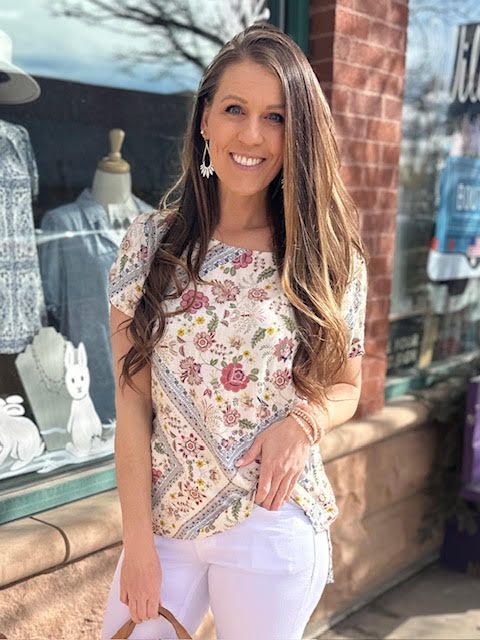 Una mujer con un top de flores y unos pantalones cortos blancos está delante del escaparate de una tienda.