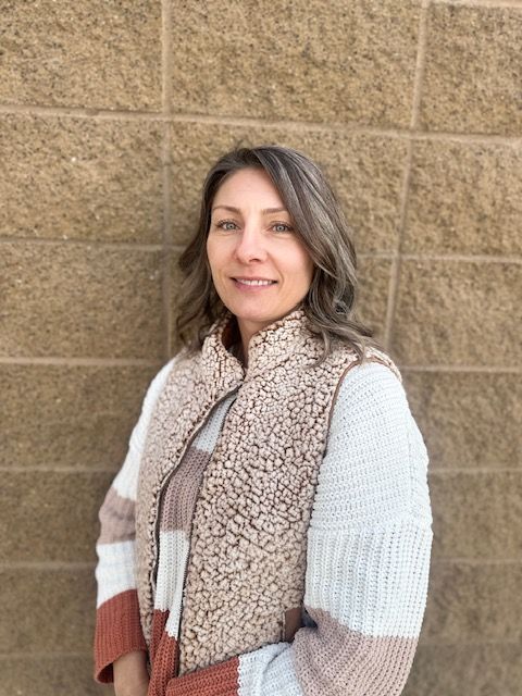 A woman in a sweater and vest is standing in front of a brick wall.