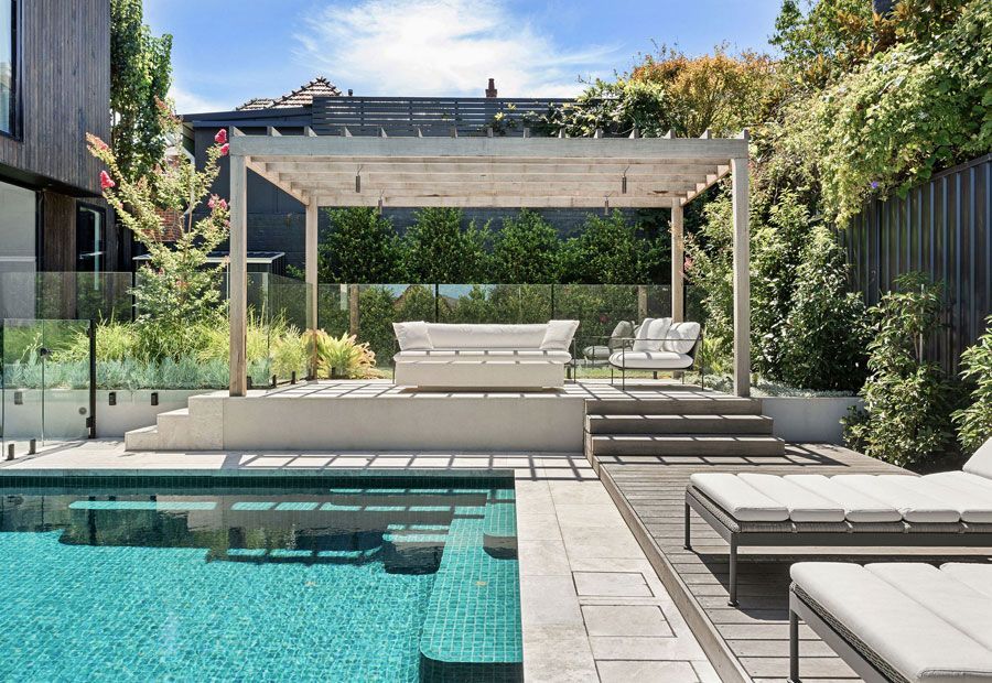 Luxury backyard pool with lounge seating under a pergola and steps leading to pool.