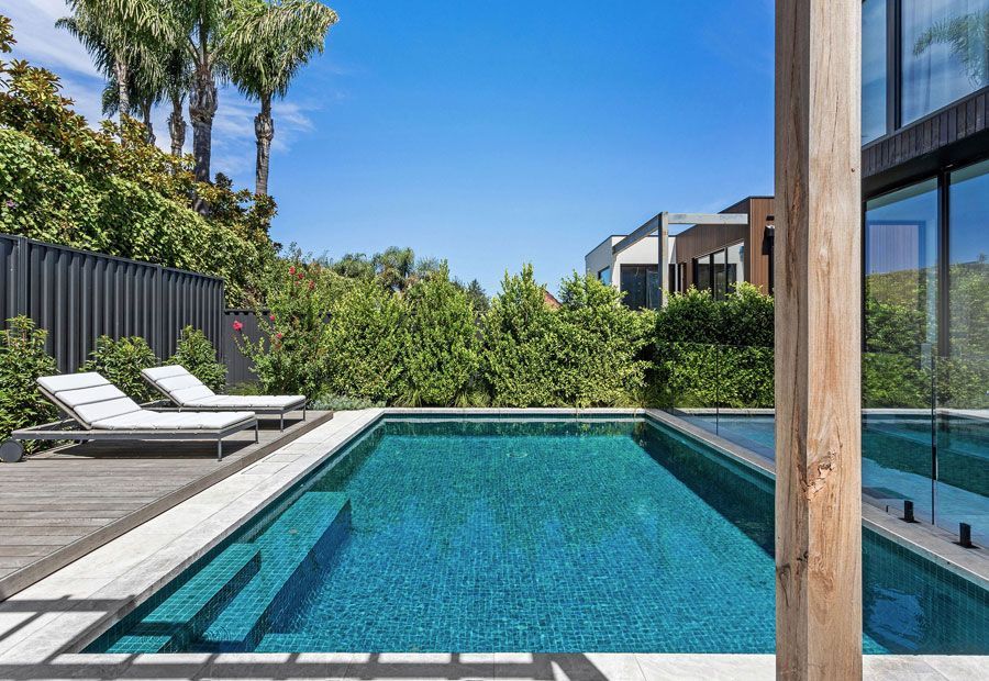 Swimming pool with turquoise water, wood deck, lounge chairs, and green trees under a blue sky.