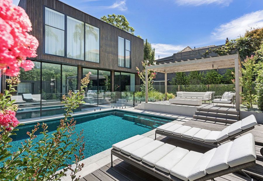 Modern home with pool, lounge area, and dark wood exterior. Sunny outdoor setting.