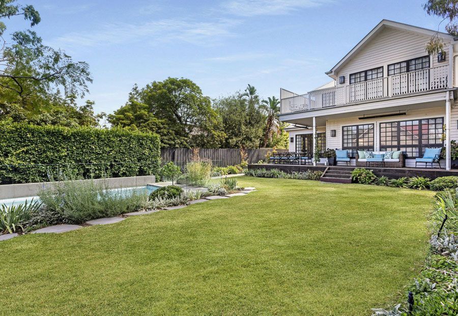 Backyard with a two-story white house, a pool, and a manicured lawn.