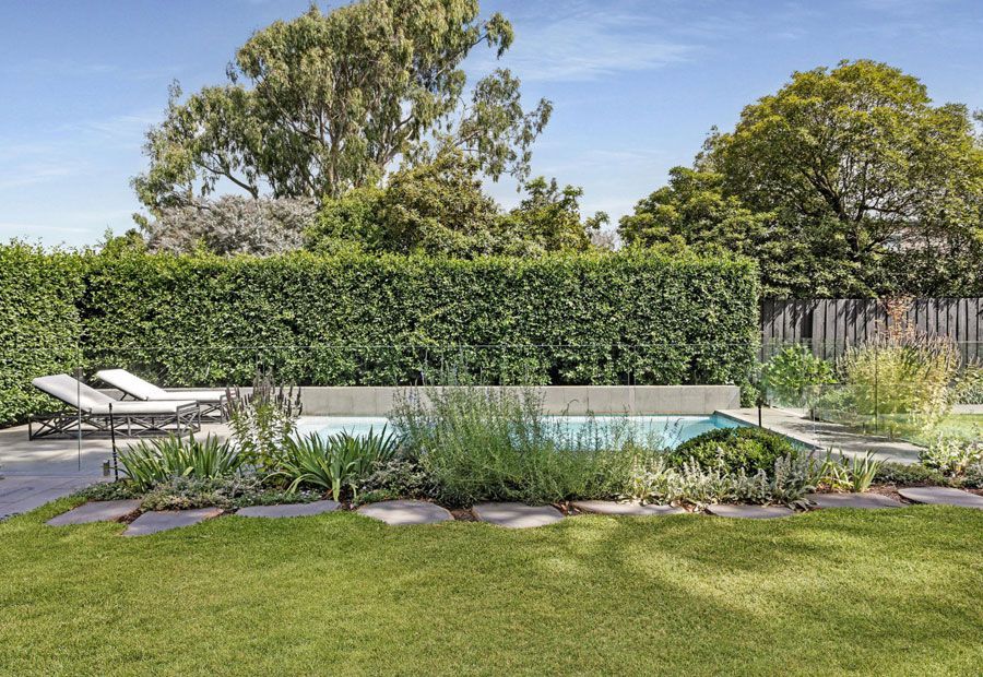 Backyard with pool, greenery, lounge chairs, and manicured lawn. Sunny day.