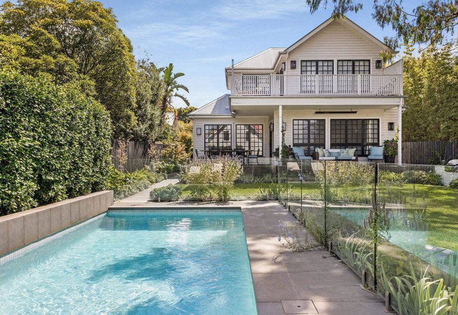 White house with a pool, glass fence, and green lawn.