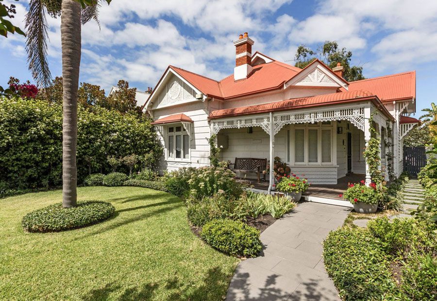 White cottage with red roof, front porch, green lawn, garden path, sunny day.