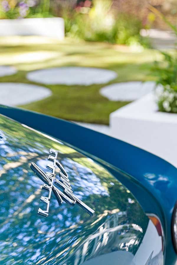 Blue car hood with a silver emblem, in a garden setting.