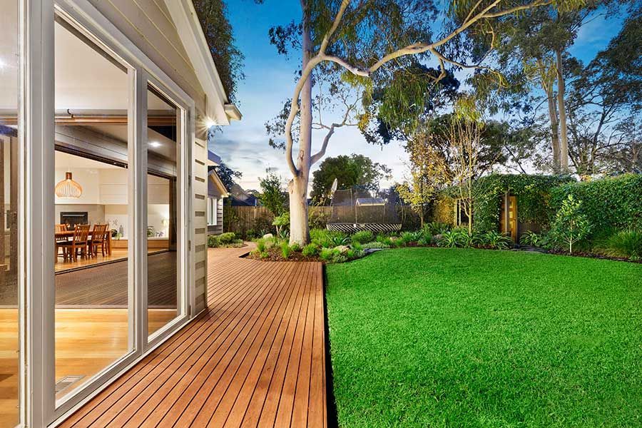 Backyard view: Wooden deck next to green lawn, with house interior visible through glass doors.