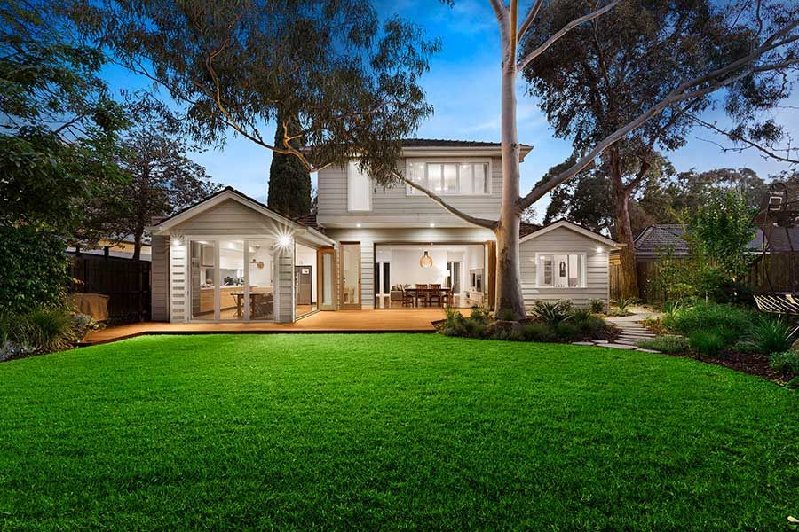 A two-story house with a large green lawn, patio, and mature trees in the backyard.