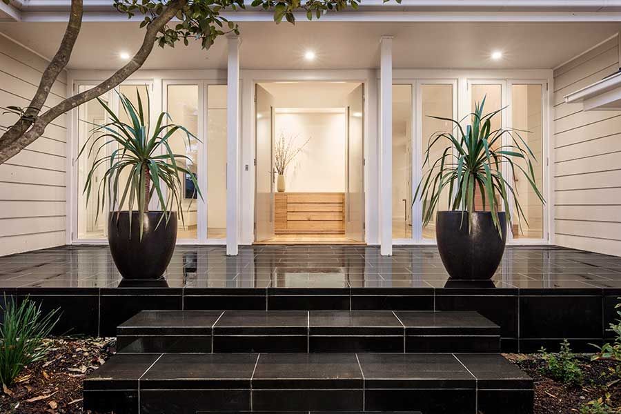 Entrance of modern house with black tiled steps and potted plants.