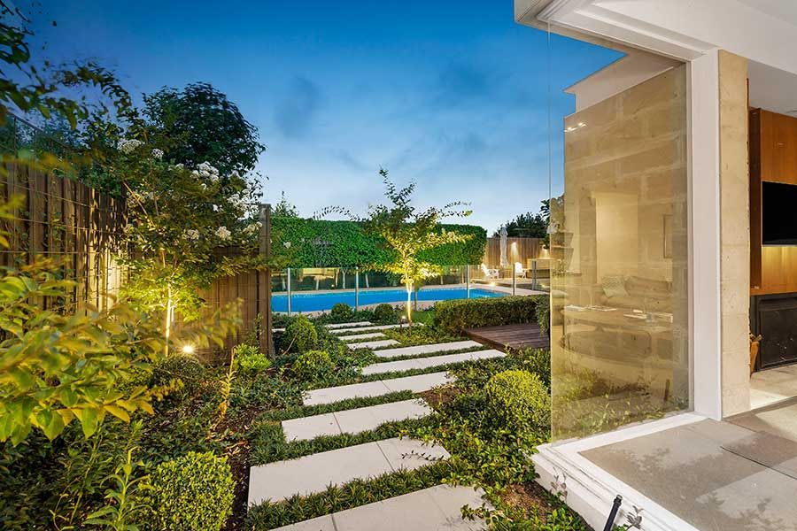 Stone path leads through a lush garden to a pool at dusk.
