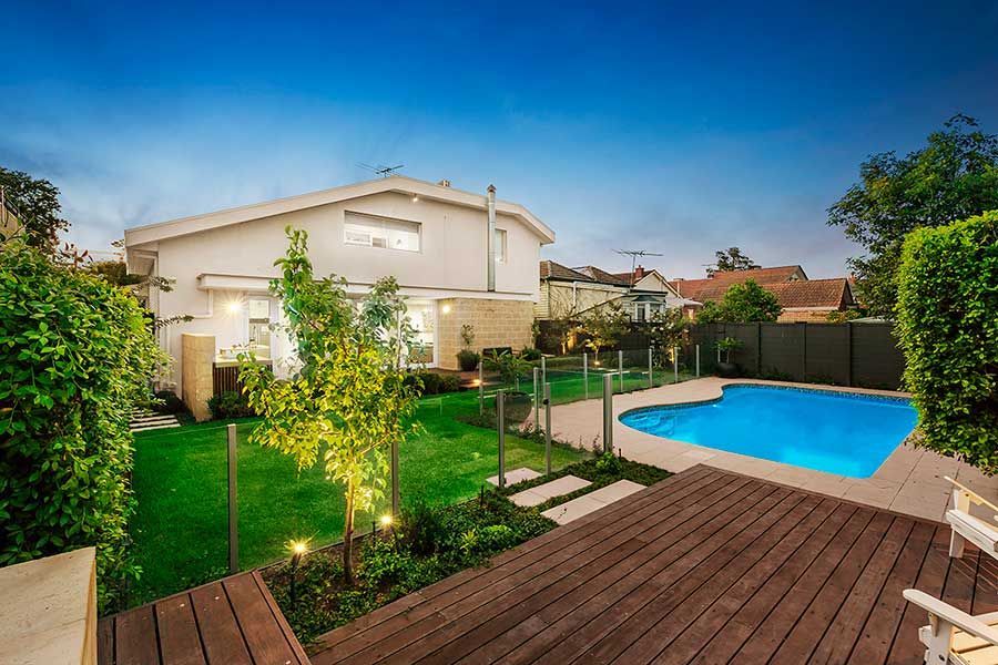 Backyard with a swimming pool, deck, and a two-story house.