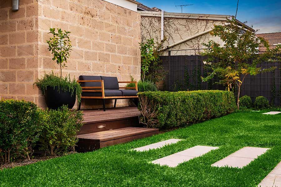 Backyard with steps to a seating area, bordered by hedges, and a lawn with stepping stones.