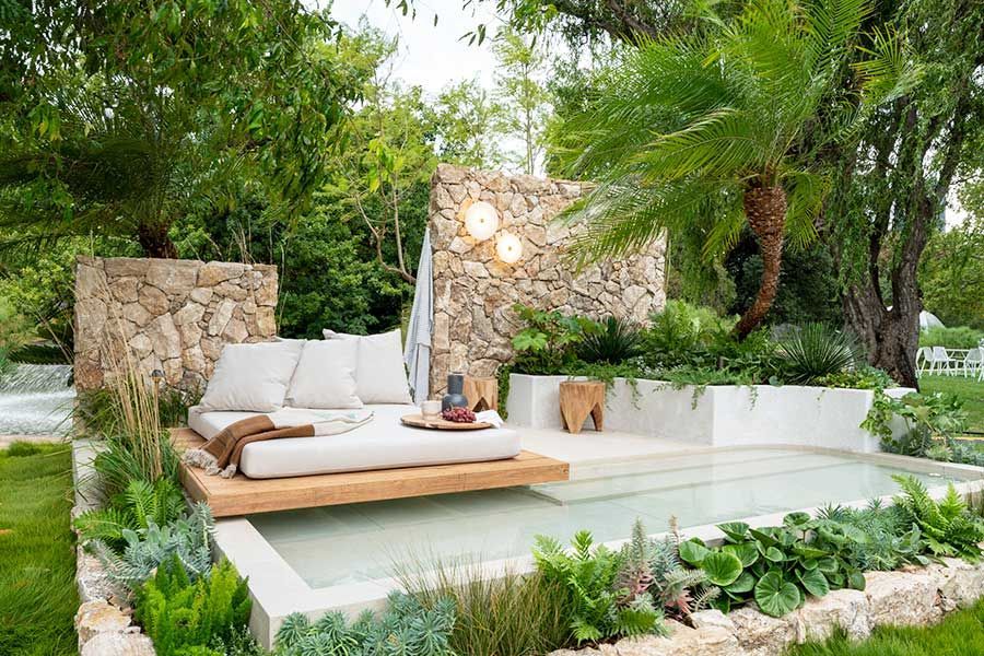 Outdoor oasis with a stone wall, daybed, and small pool surrounded by greenery.