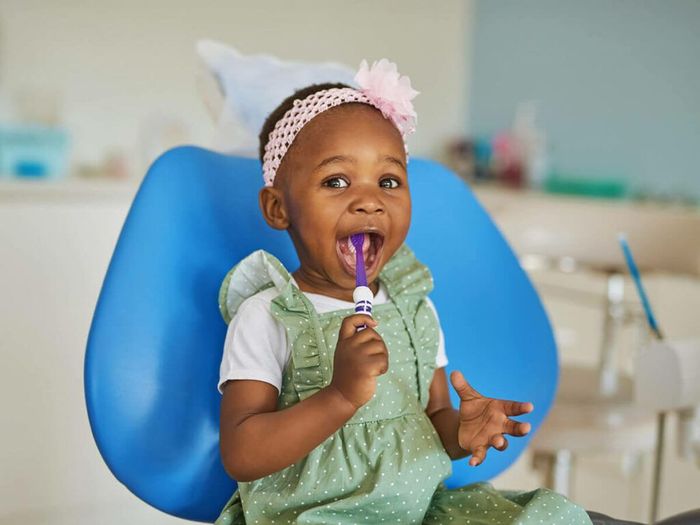 A little girl is brushing her teeth in a dental chair.