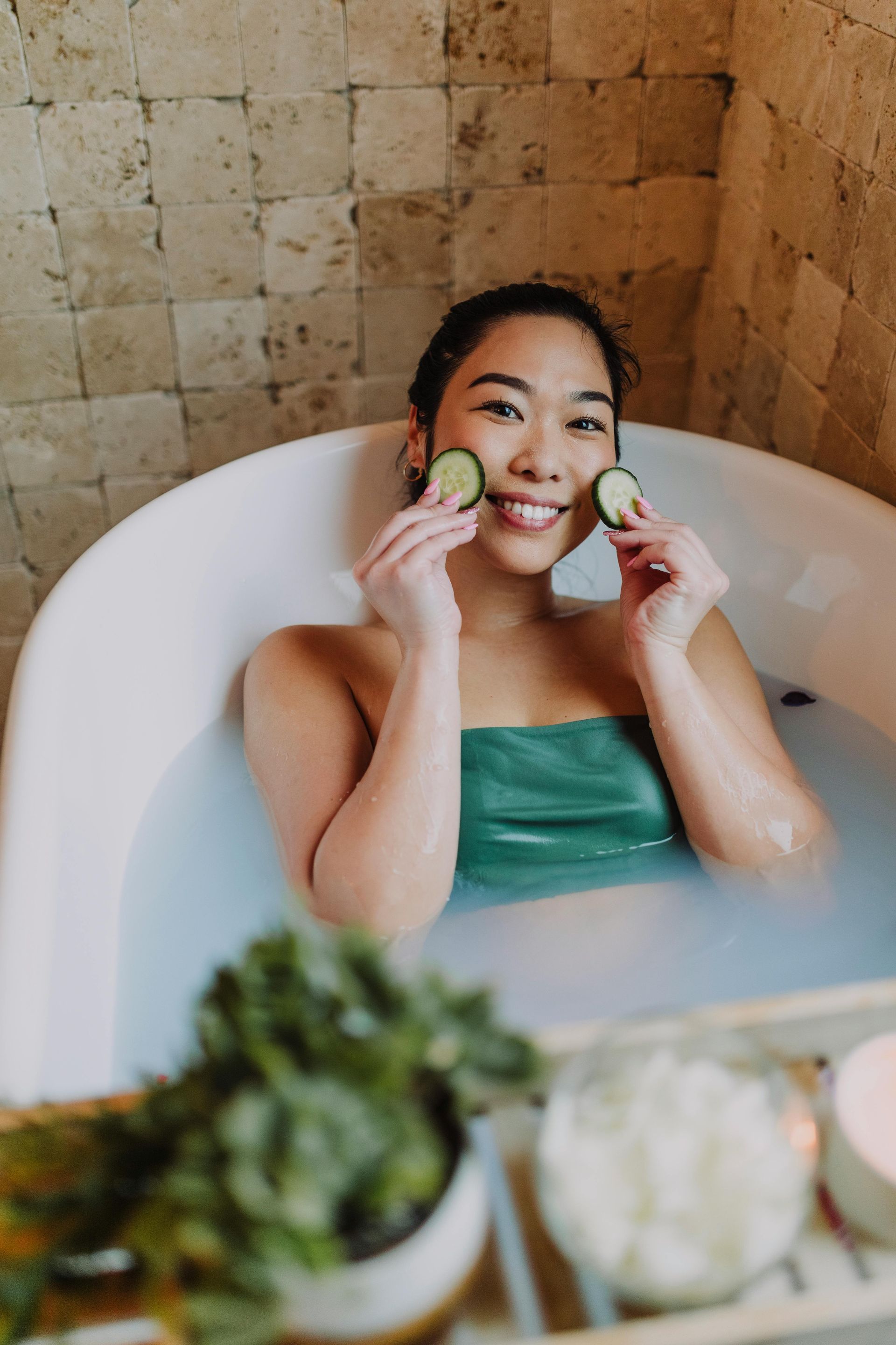 Smiling woman holding cucumber slices in a tub filled with rejuvenating waters