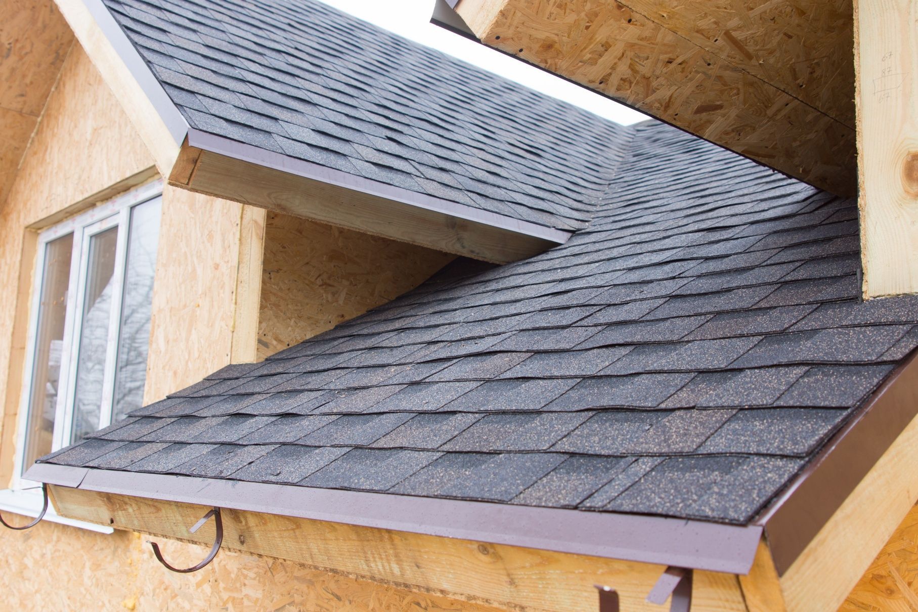 Roof with dark gray shingles on a house under construction, showing intersecting sloped sections