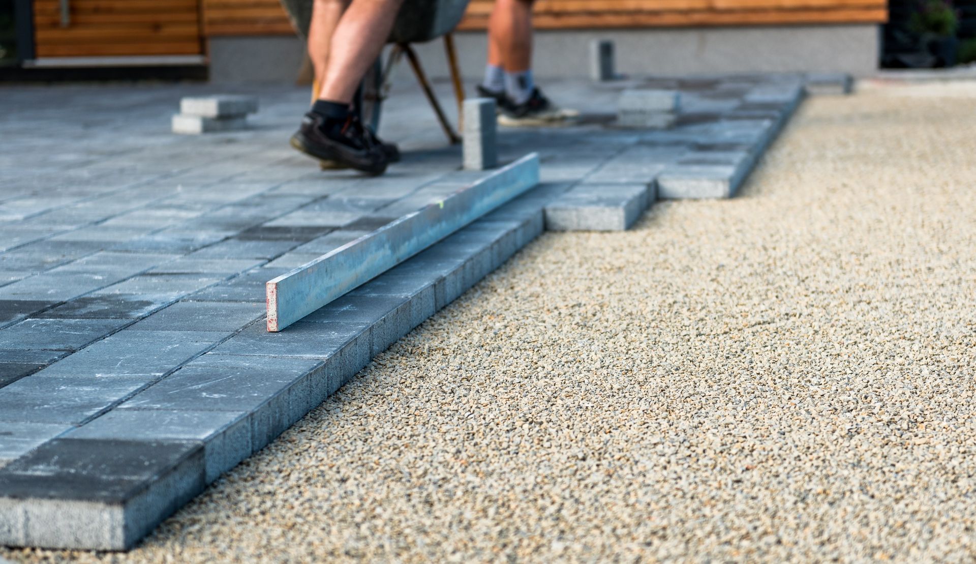 Worker installing gray paving stones on a patio beside a gravel surface