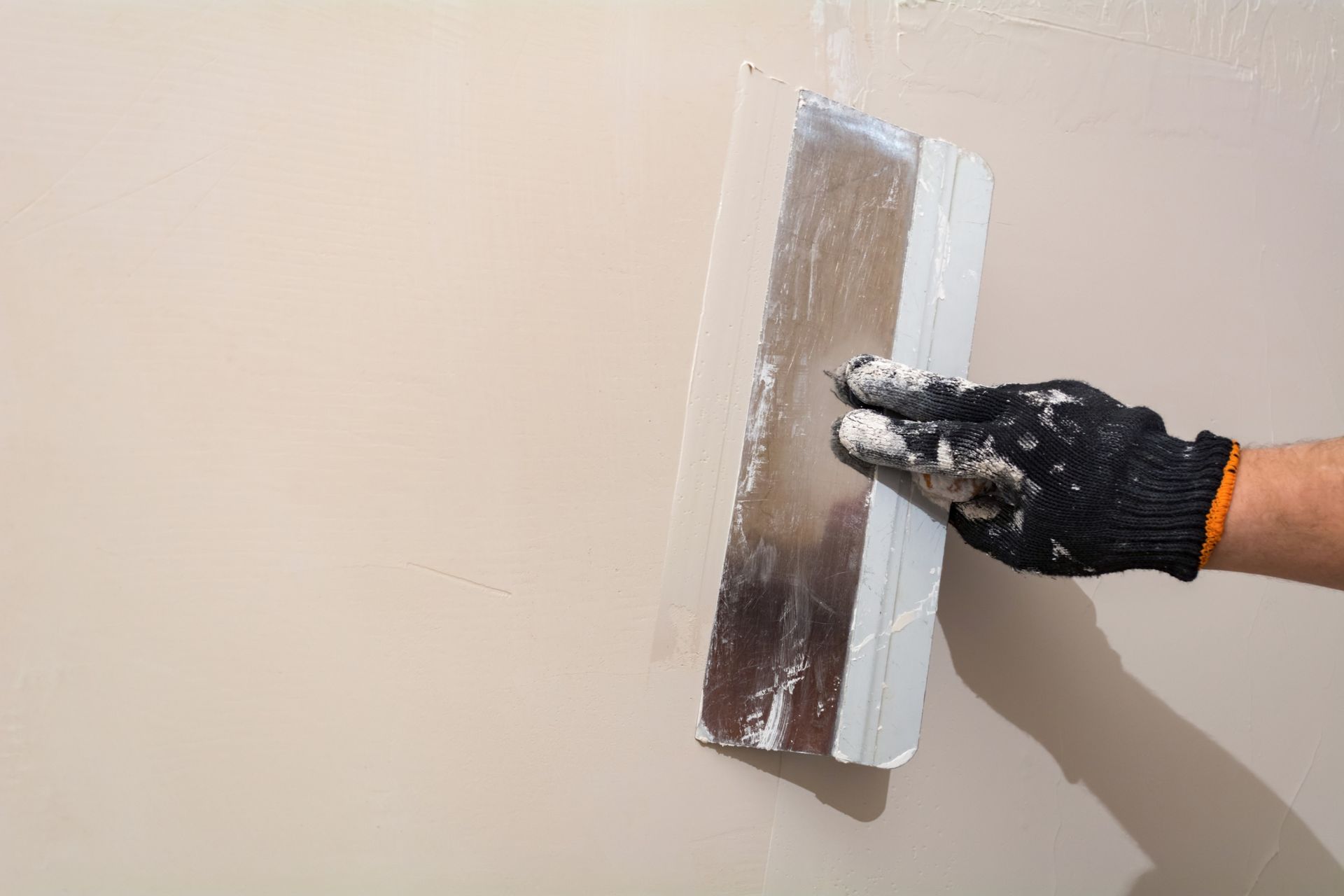 Gloved hand using a trowel to smooth beige wall plaster
