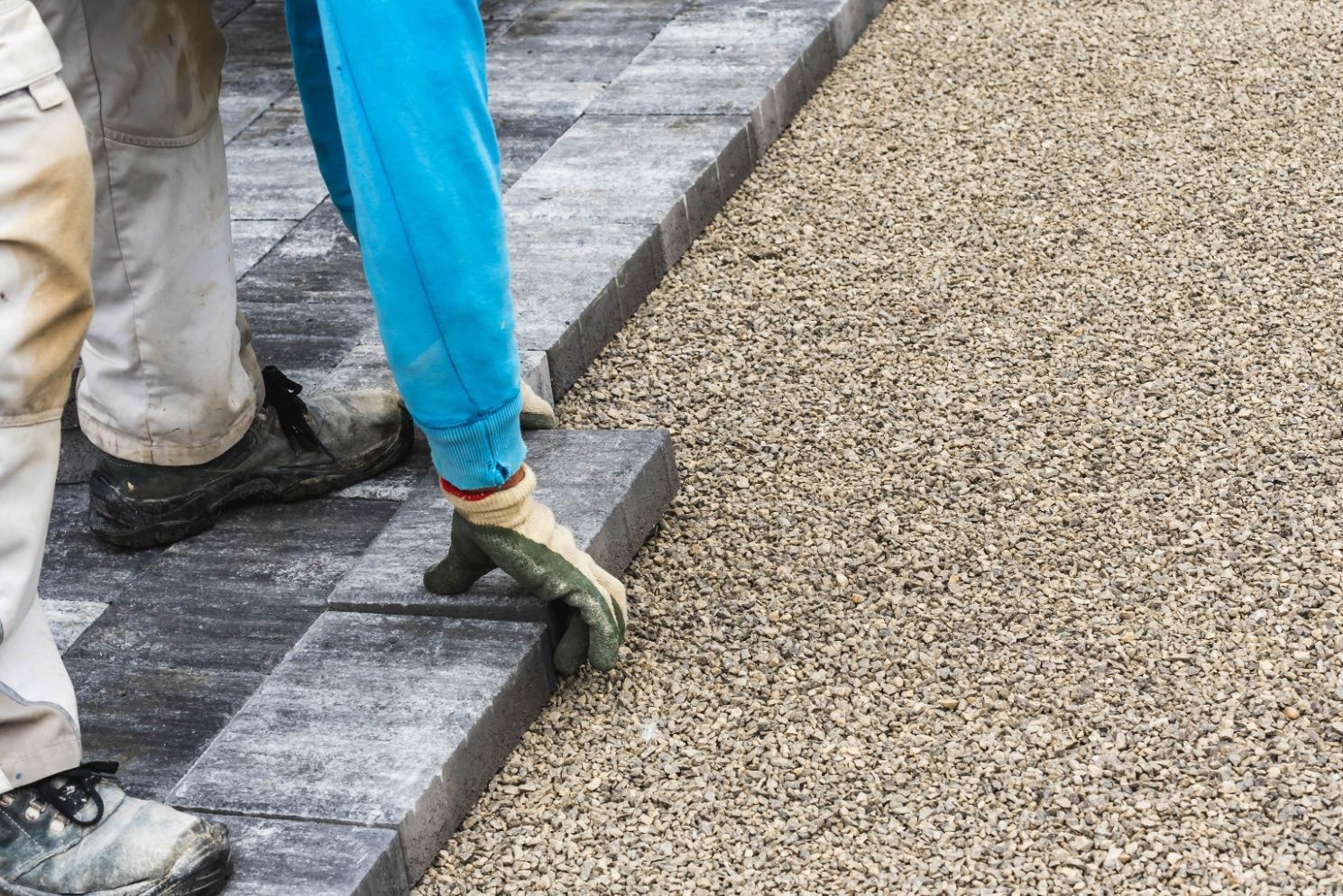 Workers paving a path, placing gray stone edging beside a gravel walkway