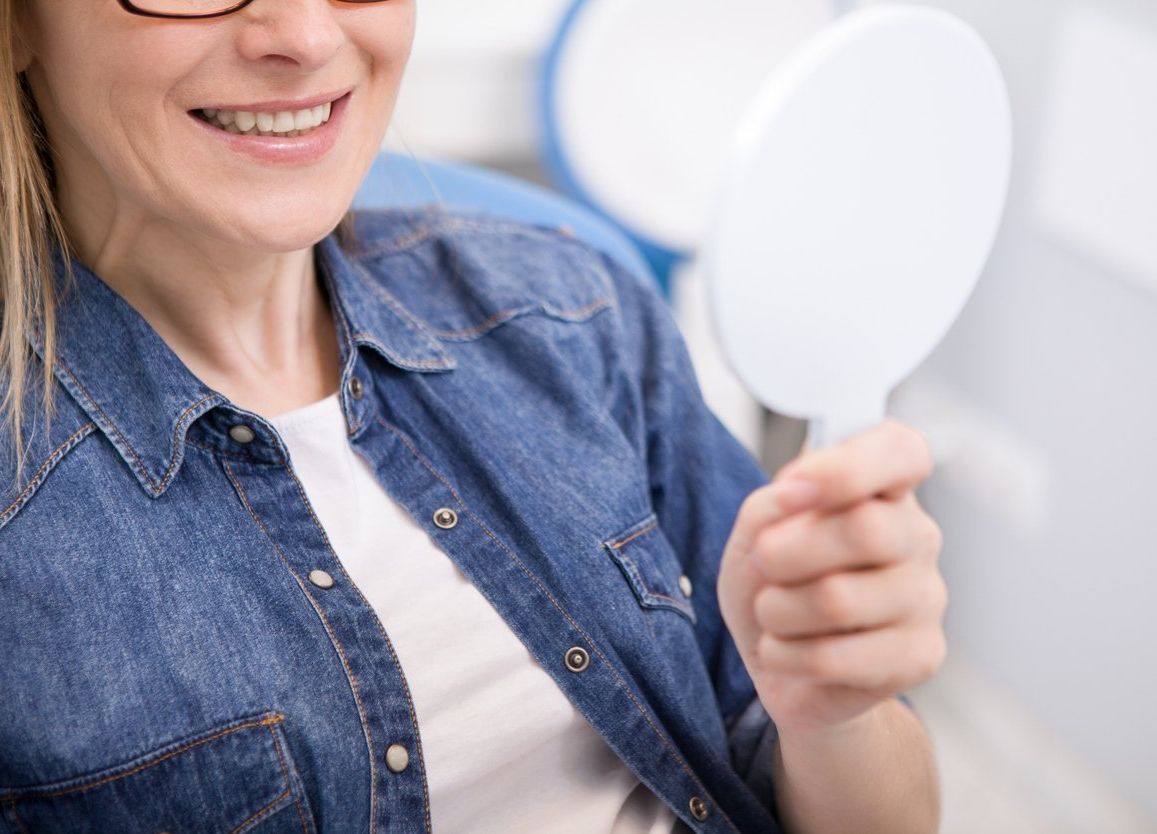 A woman is smiling while looking at her teeth in a mirror.