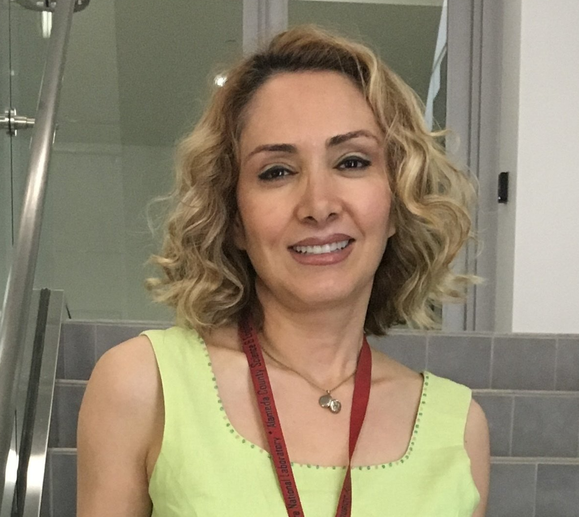 A woman wearing a yellow top and a red lanyard smiles for the camera