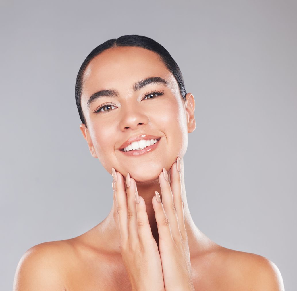 A woman is smiling and touching her face with her hands.