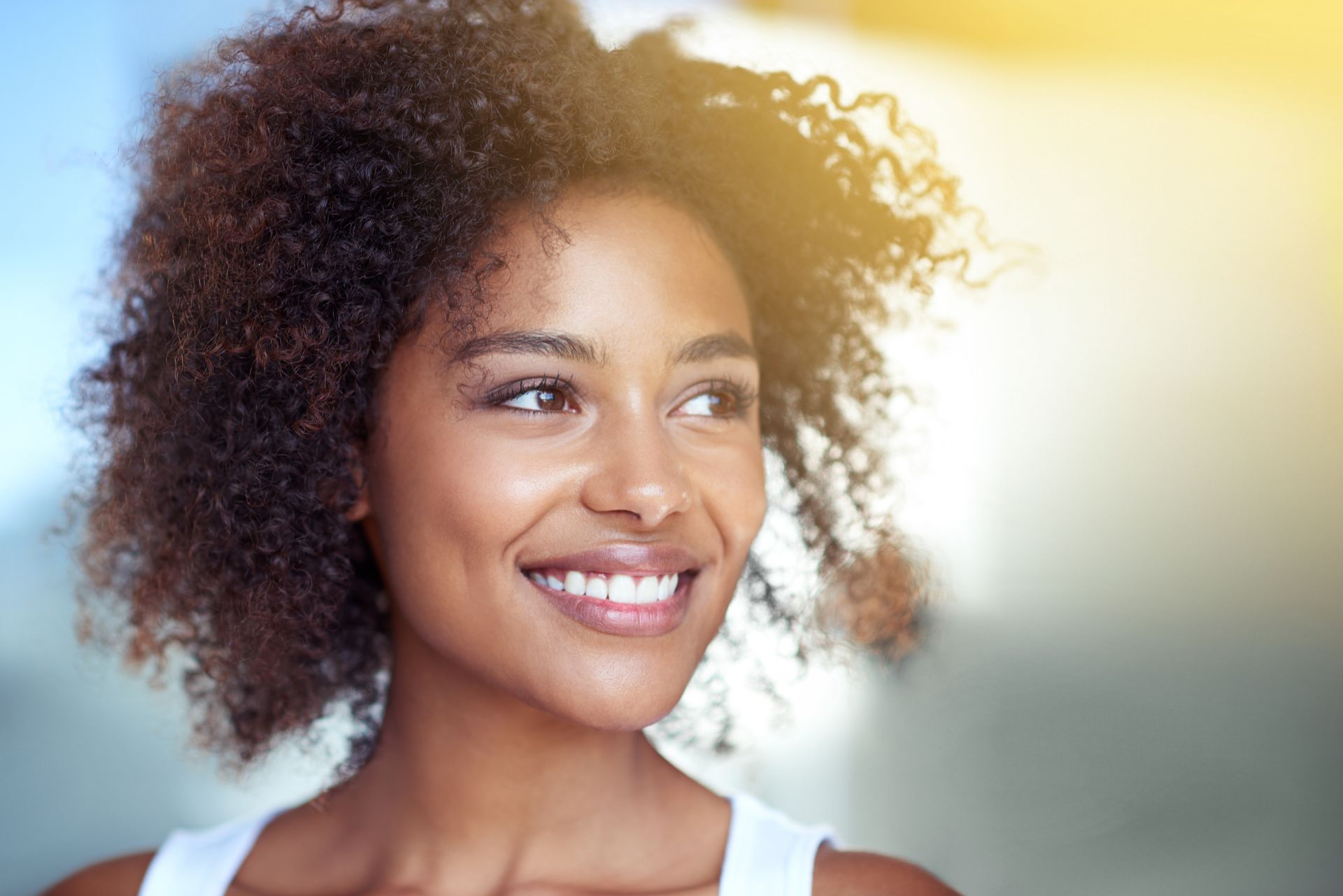 A woman with curly hair is smiling and looking to the side.