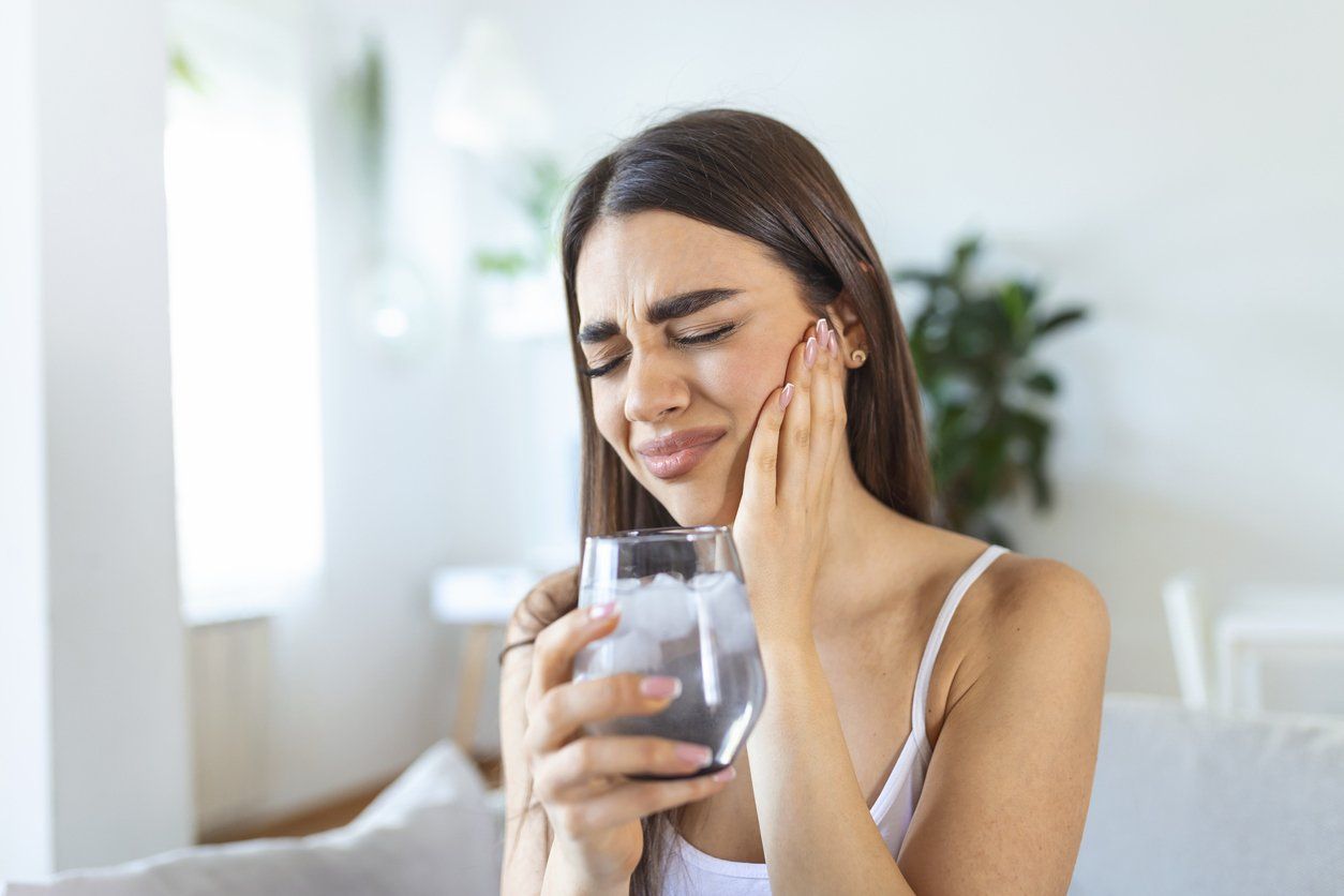 A woman is holding a glass of water with ice in her hand.