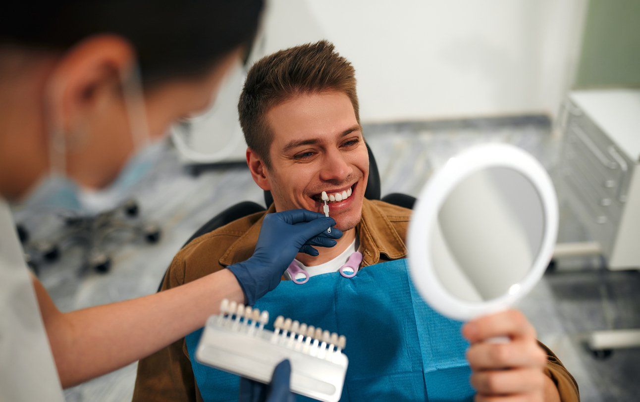 A man is sitting in a dental chair looking at his teeth in a mirror.