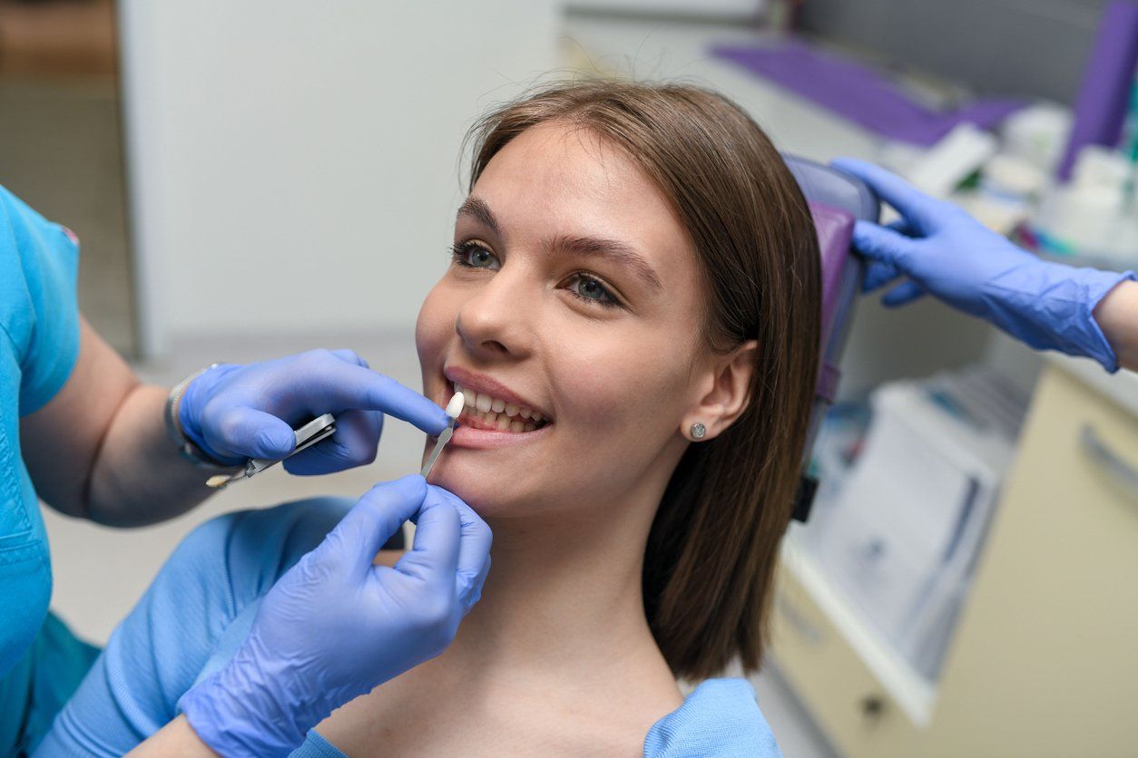 A woman is sitting in a dental chair while a dentist examines her teeth.