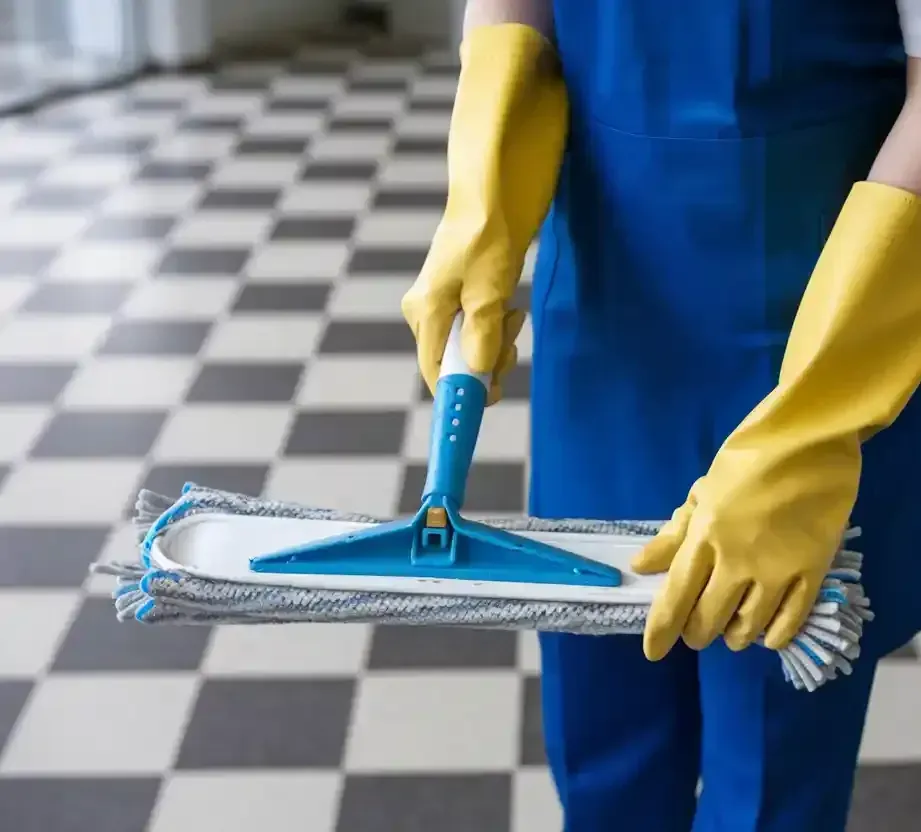 A person wearing yellow gloves is holding a mop and brush.