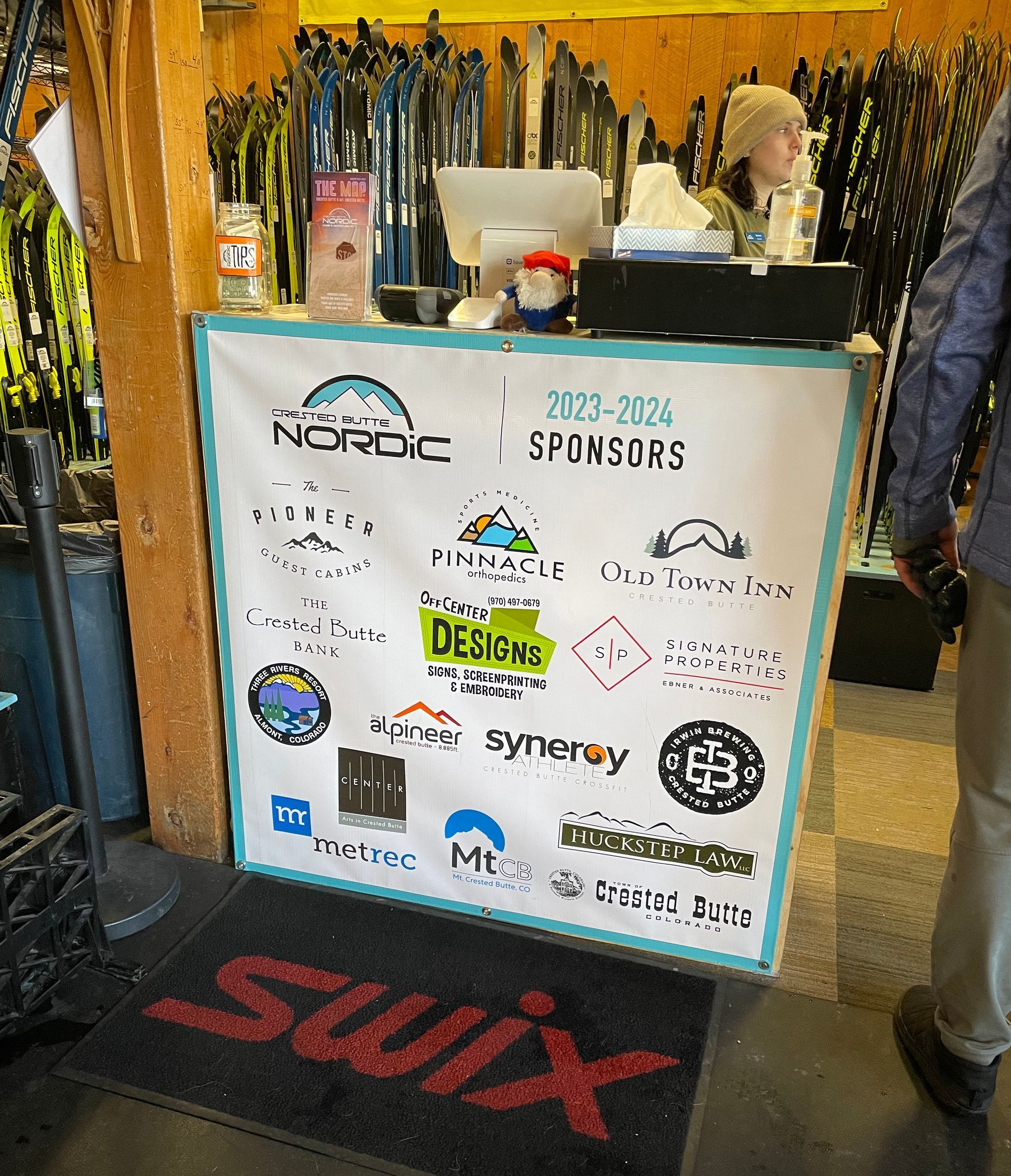 Cashier counter with sponsors' logos; person at register; skis in background;