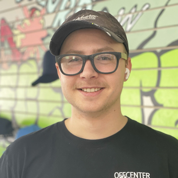 Man wearing a cap and glasses smiles, posing in front of graffiti.