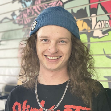 Man with long hair and beanie smiling, wearing a chain necklace and black shirt.