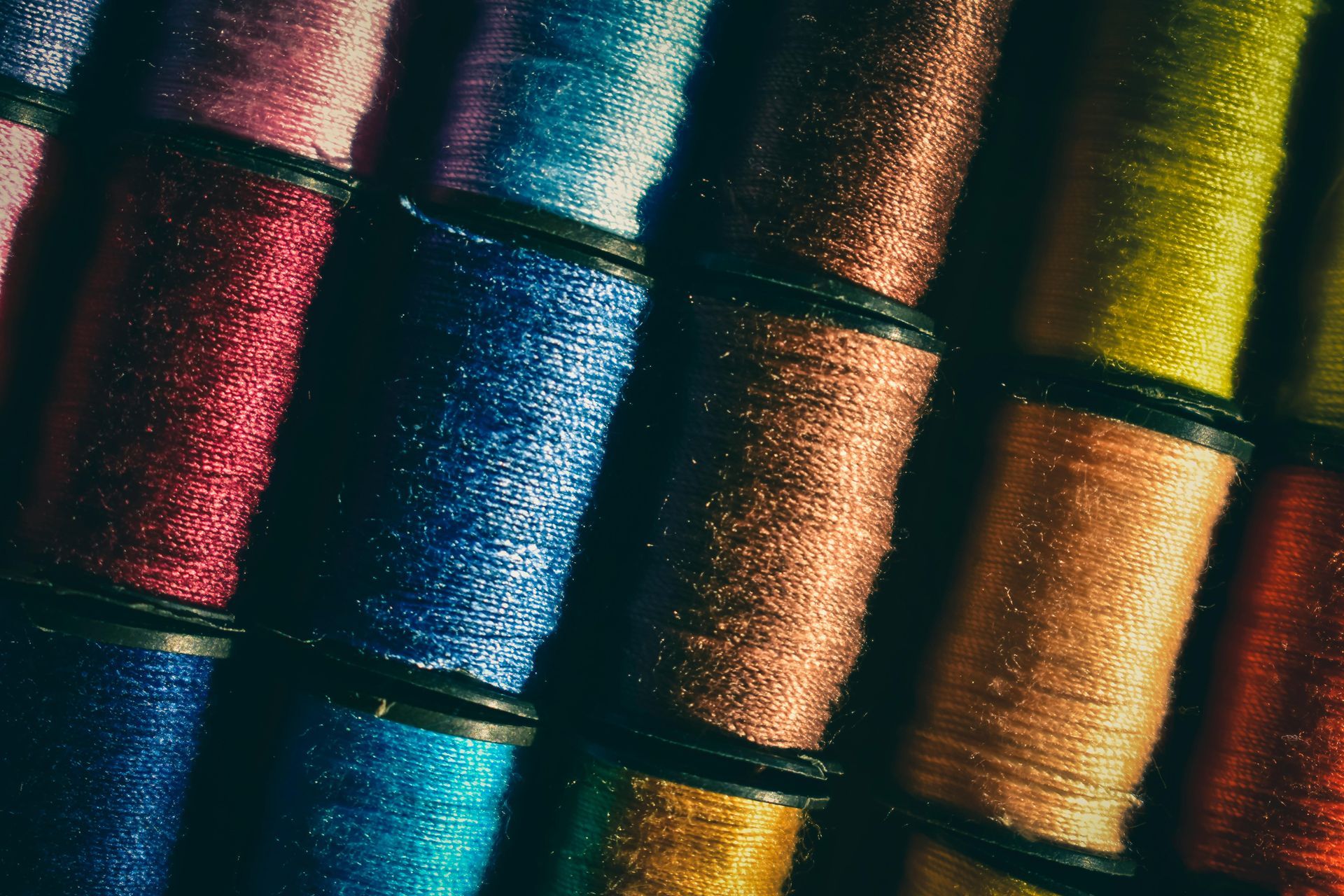 Spools of vibrant, iridescent thread in various colors, tightly wound on black plastic bobbins.