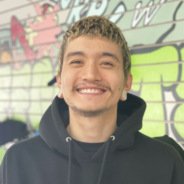 Man with blonde hair and ear gauges, smiling in front of graffiti.